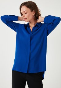 Blue button-up shirt made of smooth fabric, featuring long sleeves and a casual fit. The design includes a collar and subtle stitching details.
