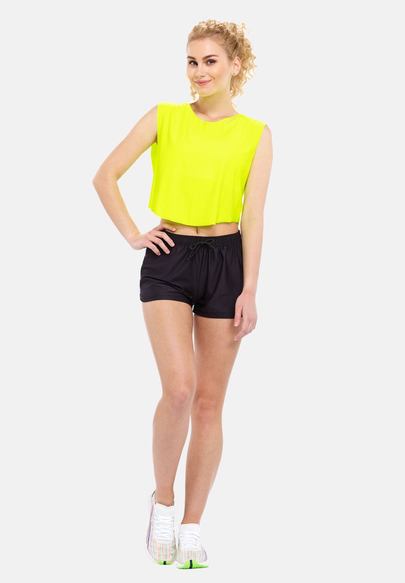Neon yellow cropped sleeveless top paired with black shorts. The outfit features a drawstring waist, with white and iridescent sneakers.