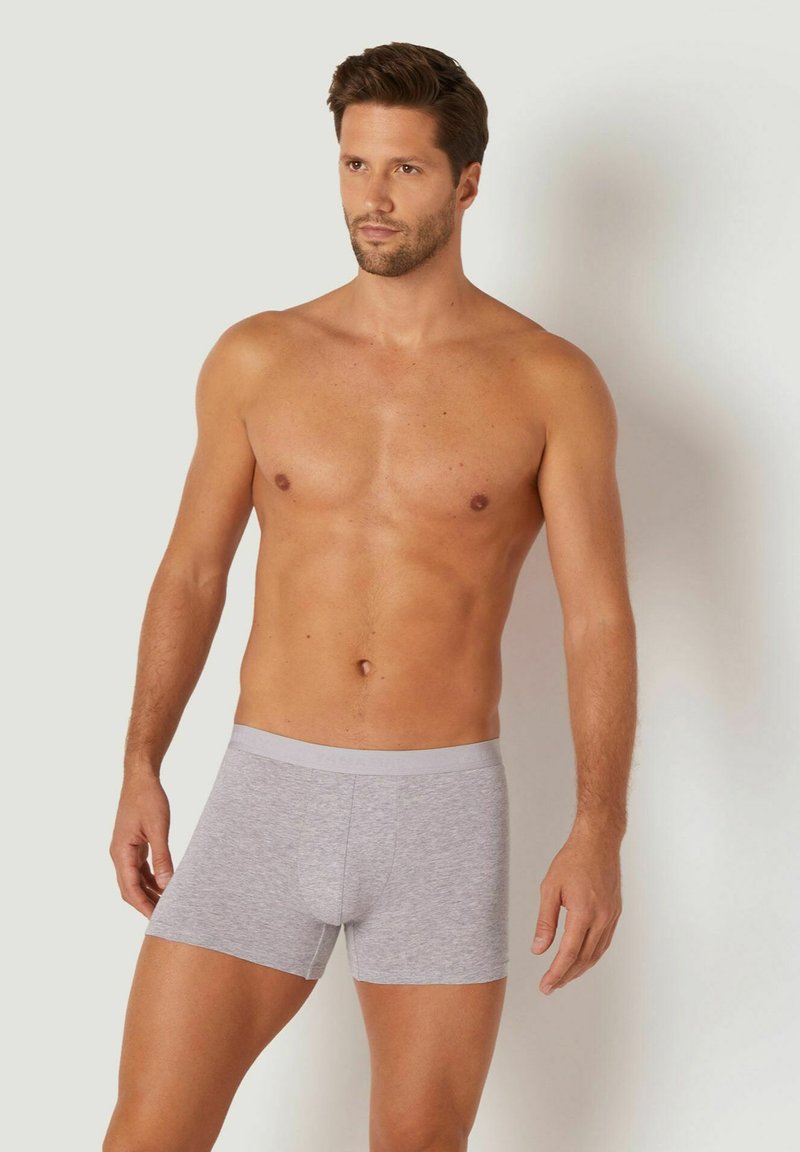 Boxeri din bumbac gri cu un talie moale și un design ajustat, purtați de un bărbat fără cămașă. Textură netedă și lungime scurtă.
