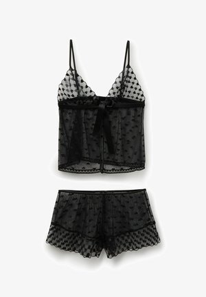 Černý průsvitný set spodního prádla se vzorem srdíček, obsahující tílko s tenkými ramínky a odpovídající šortky s vroubkovanými okraji.