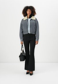Denim jacket with a sherpa collar, gray with vertical stripes, paired with high-waisted black flared pants and a black handbag.