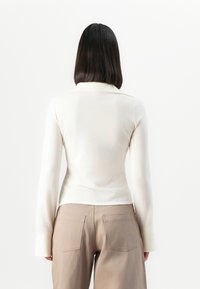 Langermet, kremfarget topp med krage, komplementert av lange ermer og en tettsittende design, parret med beige, høy midje bukser.