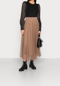 Haut noir à manches longues côtelé avec des manches bouffantes transparentes, associé à une jupe en tulle beige à pois et des bottines noires. Sac à main noir inclus.