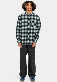 Sort og tealternet flannel skjorte med lange ærmer, knappet krave og en brystlomme; kombineret med løse sorte bukser og blå sko.