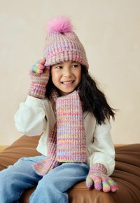 Cappello, sciarpa e guanti lavorati a maglia nei colori pastello con un pom-pom rosa soffice. Presentano una texture a coste e accenti colorati sui guanti.