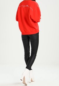 Felpa rossa con testo ricamato sul retro, abbinata a leggins in ecopelle neri e stivaletti bianchi con tacco alto.