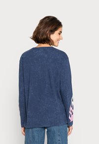 Camisa de mangas longas azul-escura com acabamento texturizado, apresentando gráficos de chamas rosas nas mangas. Decote redondo e ajuste descontraído.