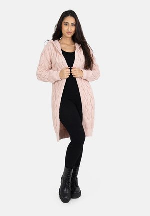 Longue cardigan rose en tricot torsadé avec capuche, ouvert sur le devant et à poignets côtelés, associé à des leggings noirs et des bottes de combat noires.
