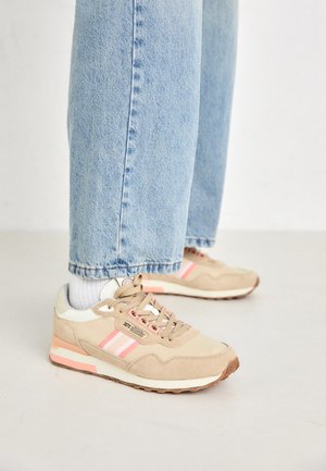 Beige suede sneakers with pink stripes, white accents, and a rubber sole. Worn with light blue cuffed jeans and white socks.