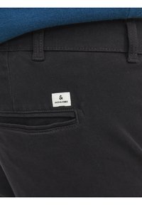 Gros plan sur un pantalon noir avec une poche arrière et une étiquette blanche de la marque Jack & Jones au-dessus du bord de la poche.