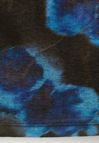 Gros plan d'un tissu avec un motif tie-dye bleu et noir montrant une texture tricotée et un ourlet cousu en bas.