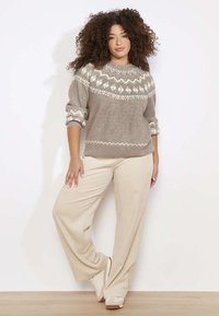 Hellbrauner Strickpullover mit weißem geometrischem Muster am Ausschnitt, kombiniert mit beigen, weit geschnittenen Cordhosen und beigen Schuhen.