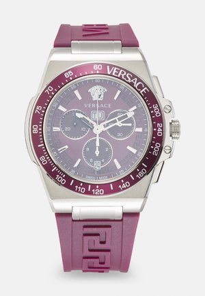 Ceas cu bratara din cauciuc mov, carcasă din oțel inoxidabil argintiu, față rotundă, cadrane de cronograf și logo-ul Versace. Dispune de un model cu cheie grecească.