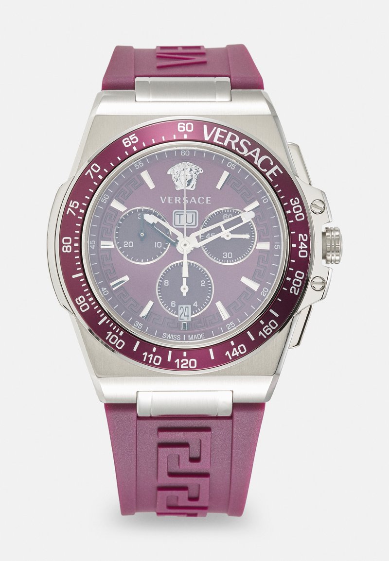 Lilla kummirihmaga kell, millel on hõbedane roostevabast terasest korpus, ümmargune kellanägu, kronograafide dials ja Versace logo. Omab Kreeka võtme mustrit.