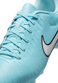 Világoskék szintetikus focicipő texturált felsőrésszel, fekete Nike swoosh logóval, fehér fűzősorral és perforált részletekkel a nyelvén.
