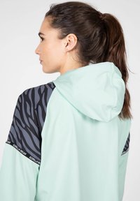 Sudadera de color verde menta claro con un diseño de rayas negras y grises en los hombros. Incluye una capucha con cordón y acentos de logo.
