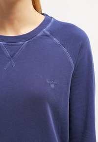 Navy blauwe pullover sweatshirt van een zachte katoenmix, met een geribbelde ronde hals, raglanmouwen en een reliëf merklogo op de borst.