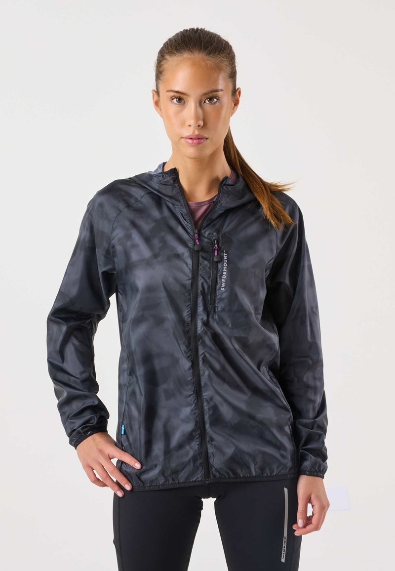 Černá lehká bunda s maskáčovým vzorem, celopropínací zip a kapucí. Má elastické manžety a malý logo na přední straně.