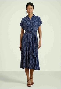 Tumši zilā auduma apģērbs ar ģeometrisku baltu rakstu, īsām piedurknēm un saitētu jostas jostu. Svārki plūst līdz ceļgala vidum.