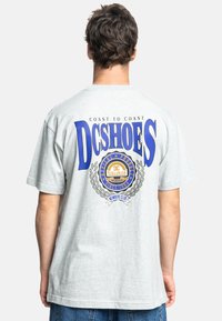 Gray cotton t-shirt featuring a large blue "DCSHOES" logo and a circular graphic with laurel accents on the back. Casual fit and short sleeves.