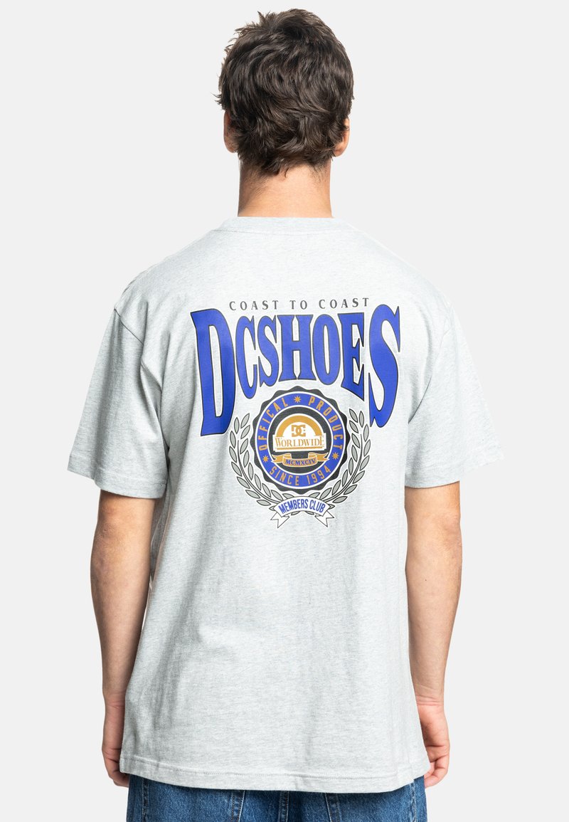 Gray cotton t-shirt featuring a large blue "DCSHOES" logo and a circular graphic with laurel accents on the back. Casual fit and short sleeves.