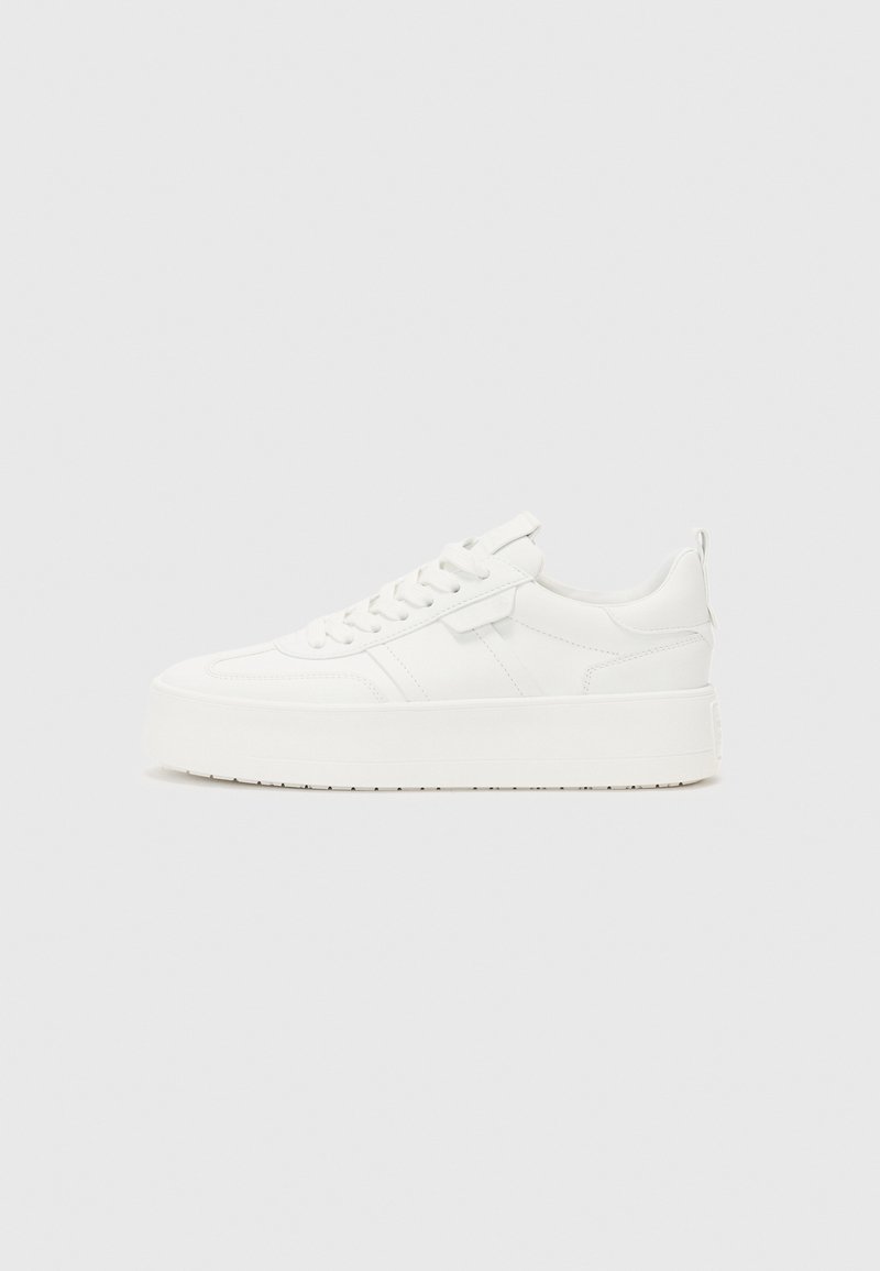 Sneaker blanche avec une tige en cuir lisse, bout rond, lacets plats et semelle compensée épaisse. Présente des coutures discrètes et une languette au niveau du talon.