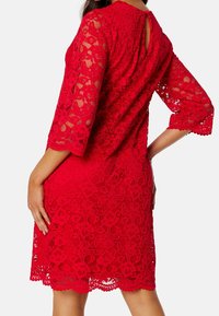 Robes en dentelle rouge avec des manches trois quarts, motif floral, ourlet festonné et détail de dos en trou de serrure, mettant en valeur un savoir-faire complexe.