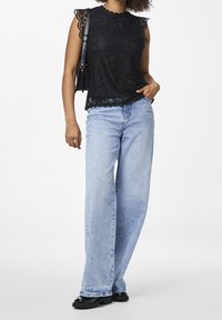 Top senza maniche in pizzo nero con bordi ondulati abbinato a jeans a gamba larga blu chiaro a vita alta e scarpe nere chunky.