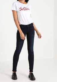 Vit t-shirt med röd text, tillsammans med mörkblå skinny jeans. Svarta skor fulländar outfiten. Slätt tyg med figursydd silhuett.