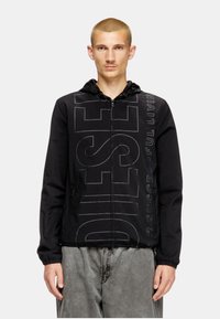 Veste zippée noire avec capuche, arborant un grand texte "DIESEL" en noir légèrement plus clair. Fabriquée en matériau léger et texturé.