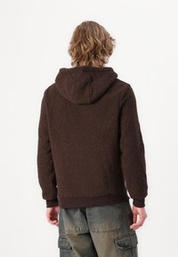 Rudas hoody, pagamintas iš pūkuotos medžiagos su tekstūruotu paviršiumi, su gobtuvu ir švelniais rankogaliais bei apatine juosta. Atsitiktinis dizainas su laisvu pjūviu.