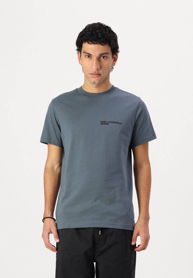 T-shirt en coton gris avec des manches courtes et un col rond. Présente un petit logo noir "Karl Lagerfeld Jeans" sur le côté gauche de la poitrine.