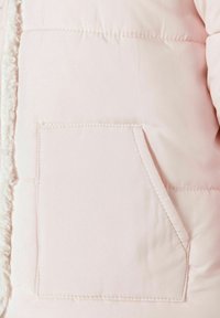 Lyserød, quiltet jakke lomme med skr�å topkant og synlige syninger, ved siden af et tekstureret indre foer.