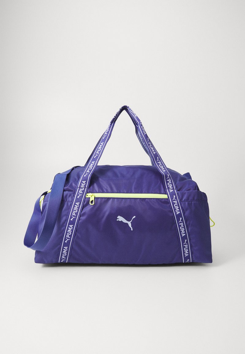 Vijolična športna torba iz teksturirane tkanine, zadrgo in belim logotipom. Ima nastavljive trakove z blagovno znamko "PUMA" in limonine dodatke.