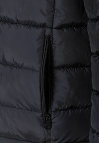 Chaqueta de plumas en un azul marino oscuro, con secciones acolchadas y un bolsillo con cremallera negra en el costado para un almacenamiento seguro. Textura suave y brillante.