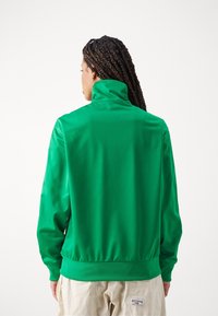 Zelená mikina s vysokým límcem, hladkým povrchem, dlouhými rukávy a elastickým lemem. Zadní pohled ukazuje přiléhavý design a minimální švy.