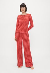Roter Schlafanzug mit Polka-Dots, bestehend aus einem langärmeligen Knopfhemd und weiten Hosen, aus weichem, leichtem Material gefertigt.