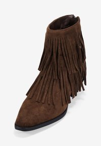 Brown suede ankle boot with fringed detail, pointed toe, and black rubber sole. Features a smooth texture and a zip closure at the back.
