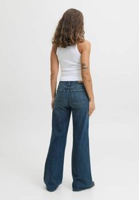 Visoke flared jeans iz temno modrega denima, z klasičnim pet-pocket dizajnom in kontrastnim šivanjem, prikazani s hrbtne strani.