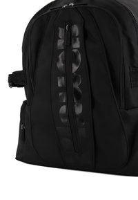 Zaino in nylon nero con una grande tasca frontale con zip e logo opaco, spallacci laterali regolabili e superficie liscia.