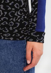 Top de manga larga de punto en negro con un patrón abstracto en blanco y azul; cuenta con acentos de canalé azul en los puños y el dobladillo; diseño ajustado.