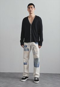 Čierny kardigán s kontrastnými gombíkmi, nosený cez multicolor patchwork nohavice z ľahkej látky. Čierne tenisky dotvárajú outfit.