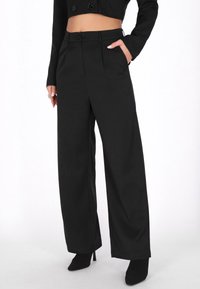 Pantaloni largi negri dintr-un material neted, având talie înaltă, cu două buzunare frontale și două nasturi, asortați cu tocuri negre.