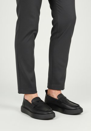 Crne cipele bez vezica s glatkim kožnim završetkom, okruglog dizajna, teksturiranim gumiranim potplatom i diskretnim ukrasnim šavom.