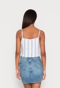 Kvinna med långt hår klädd i en ärmlös topp med blåa och vita ränder samt en blå denim mini kjol, sedd bakifrån.