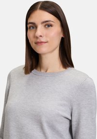 Hellgrauer Strickpullover mit rundem Ausschnitt, langen Ärmeln und subtiler Textur. Der Stoff wirkt weich und leicht.