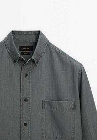 Chemise grise boutonnée avec une poche poitrine et un col boutonné, présentée sur un fond blanc uni.
