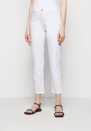 Jeans blancos recortados con un corte recto, que presentan un cierre de cremallera, botón y bolsillos frontales. Combinados con sandalias planas negras con tiras.