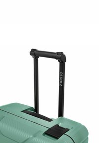Valigia rigida verde con manico telescopico nero esteso e chiusura a scatto su sfondo bianco.