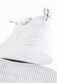Sneaker bianco in pelle con superficie liscia, punta arrotondata e suola testurizzata con motivi orizzontali e esagonali; include un linguetta sul tallone.